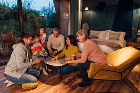 A multi-generational family sitting together on the floor and armchair in a cozy room, enjoying a card game around a coffee table