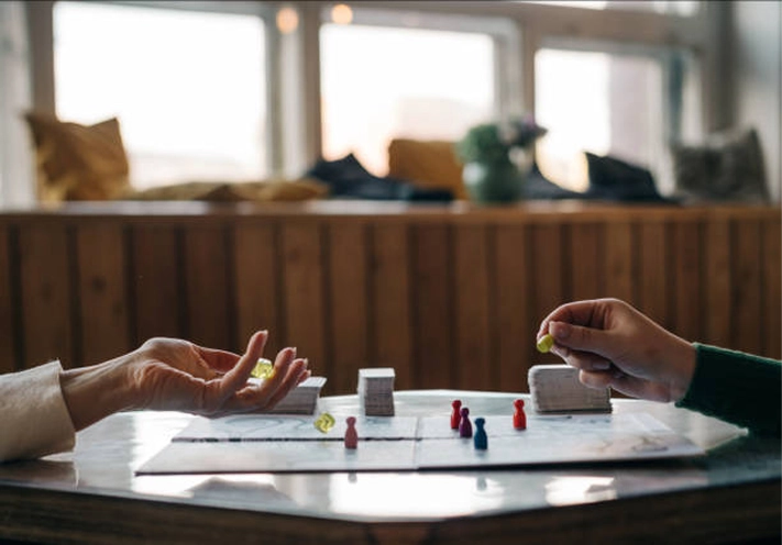 Close-up shot of two people playing a board game with colorful game pawns and rolling yellow dice on a table